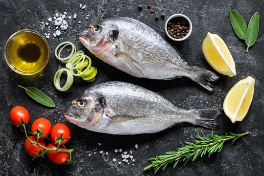 Sea bream or dorado sea fish, olive oil, spices herbs and cooking ingredients on dark slate background. Top view. Mediterranean cuisine, healthy eating, healthy cooking concept
