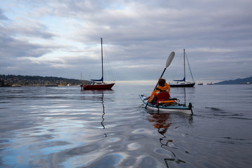 Adventurous woman is kayaking on a sea kayak during a vibrant morning. Taken in Vancouver, British...