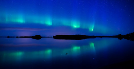 Northern lightd dancing over calm lake in Farnebofjarden national park in Sweden.