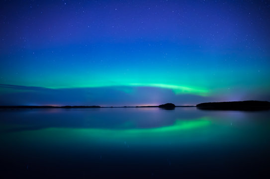 Northern lightd dancing over calm lake in Farnebofjarden national park in Sweden.
