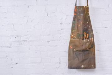 brown apron with paint brushes hanging on white brick wall