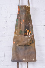 brown apron with paint brushes hanging on brick wall