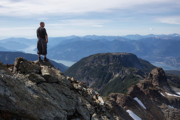 Adventurous man standing on top of a rocky mountain. Taken on Skypilot Peak, Near Squamish, North of Vancouver, British Columbia, Canada.