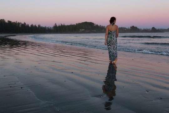 Woman Walking on a Sandy Beach during a vibrant and colorful summer sunset. Taken in Tofino, Vancouver Island, BC, Canada.