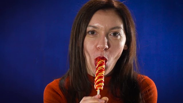 Beautiful woman is sexually eating lollipop on a blue background.