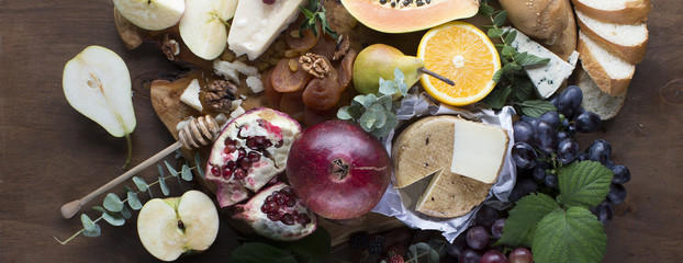 Obraz na płótnie Canvas Variety of fresh fruits, sweets and cheeses shot from above an wooden board