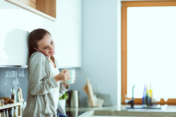 Woman using mobile phone sitting in modern kitchen.