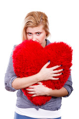 Sad girl holding big red pillow in heart shape