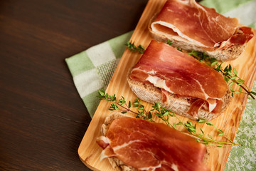 Sandwiches made from hand-made rye bread and thin chopped fresh bacon. Fresh green thyme on a wooden board. Succulend bacon on a wooden table.