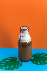 cold coffee in the bottle with drops of chocolate syrup and paper monstera leaves