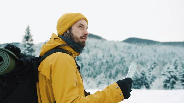 Beautiful mountains in winter time. A guy with beard, wearing yellow winter clothes is wandering and holding a map in his hands, against the background of the winter landscape