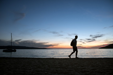 An adult man walks to the beach at the sunset in the summer