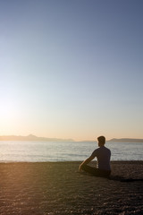 An adult male meditating on the beach at the seashore in the morning