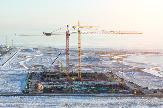 Cranes at the construction site on the shore of the snow of the frozen sea in winter.