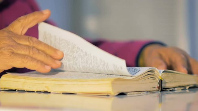 Closeup of a grandmother eighty-three years old slowly turn the pages of the book, sitting at the table.