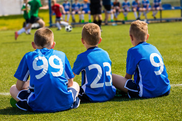 Children Soccer Team Watching Football Match. Children Sport Team in Blue Shirts. Youth Soccer School Tournament for Children. Young Boys in Soccer Jersey. Football Bench in the Background