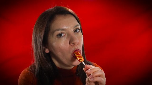 Sensual European model erotic sucks candy. Studio, red background.