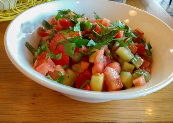 Big white ceramic bowl with fresh vegetable salad made of tomato, cucumber and parsley - on wooden table at restaurant