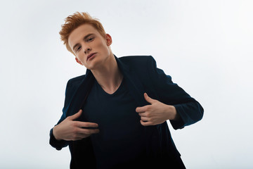 Hunk. Attractive unsmiling red-haired young man putting his jacket on and staring and having a...