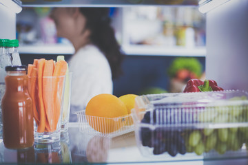 Portrait of female standing near open fridge full of healthy food, vegetables and fruits. Portrait of female