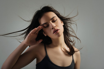 Closing eyes. Attractive unsmiling dark-haired young woman thinking and having her eyes closed and touching her temple