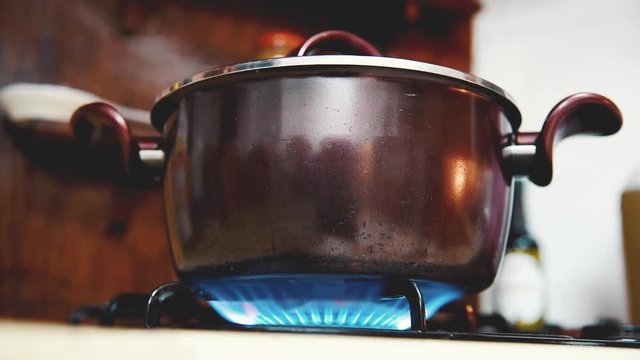 flames under coking pot in kitchen, steam release from lid
