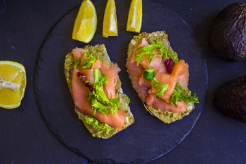morning breakfast with hot coffee and a sandwich with avocado, soft cheese, lemon and red fish trout on a dark background