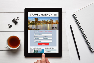 Travel agency concept on tablet screen with office objects on white wooden table. All screen content is designed by me. Flat lay