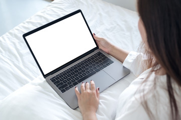 Mockup image of an Asian woman sitting on a bed , using and typing on laptop with blank white desktop screen keyboard
