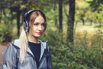 Attractive young blonde girl walking on park, listening to music on headphones.