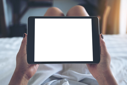 Mockup image of woman's hands holding black tablet pc with blank desktop white screen while lying in a white bed with feeling relaxed