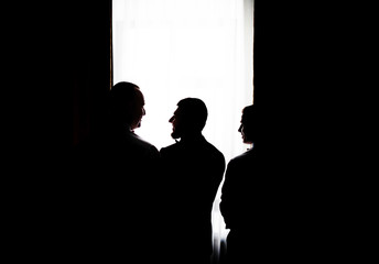 Silhouettes of three man standing before a bright window