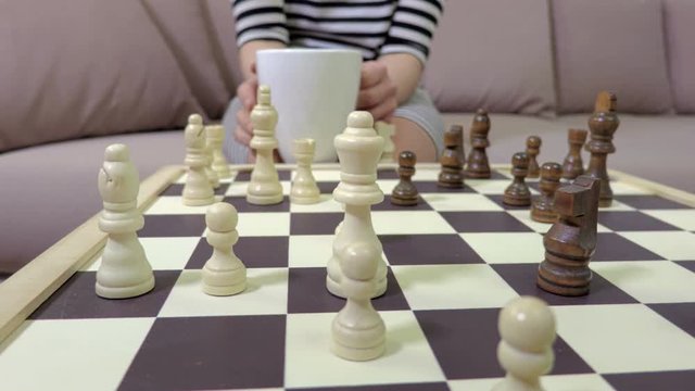 Woman with cup of tea near chessboard
