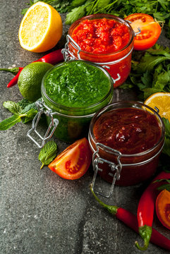 Indian traditional food, Set of three chutney for Chaat and Sev Puri - sweet date-tamarind, cilantro-mint green and red chilli garlic, On dark stone background, copy space top view