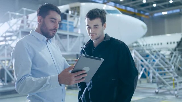 Aircraft Maintenance Worker and Engineer having Conversation. Holding Tablet. Shot on 4K UHD Camera.