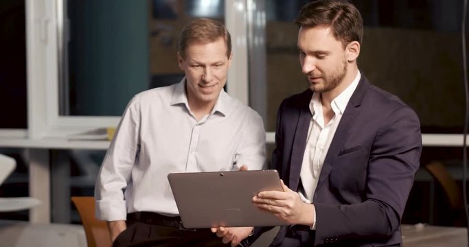 Two partners are looking at the tablet screen and discuss data of new project. Late work overtime concept.