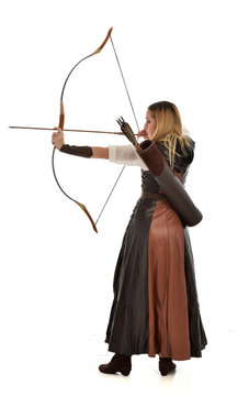 full length portrait of girl wearing brown  fantasy costume, holding a bow and arrow, on white studio background. 