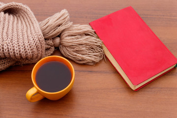 Cup of coffee, knitted scarf and book on wooden background