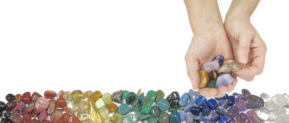 Crystal Therapy Website Banner - female hands on right side offering a selection of tumbled stones against a white background and row of chakra colored healing stones beneath   © Nikki Zalewski