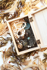 Pile of old vintage jewelry and a pocket watch in a wooden box close-up. Retro style fashion accessories for women - necklaces and pearl beads