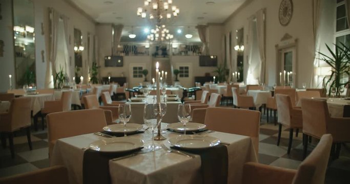 an empty restaurant hall, a table for two served candle light, ready to receive guests, dolly shot