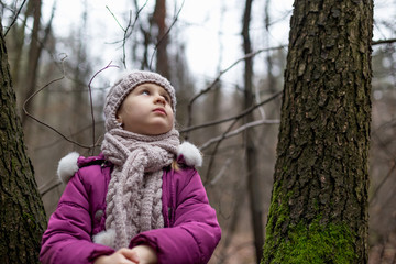 Little girl sitting near a tree in an autumn forest