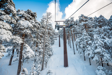A winter view of a ski resort full of fresh snow taken from the chairlift going through a forest,...