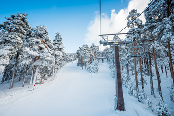 Obraz premium A winter view of a ski resort full of fresh snow taken from the chairlift going through a forest, in Madrid, Spain