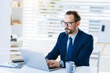 Fototapeta premium Modern technology. Handsome professional appealing businessman typing response while sitting and looking at the screen 