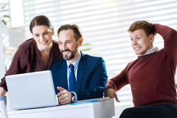  Huge profit. Ambitious pretty three colleagues gazing at the screen while grinning and man touching his head