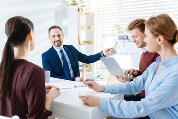 Fototapeta premium Be ready. Appealing pleasant four colleagues sitting at the table while working and man pointing at scheme