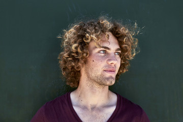 Portrait of smiling young man with curly hair in front of a green wall