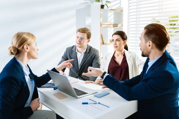 New business style.  Surprised young female colleague telling news while her colleagues sitting at the table and listening