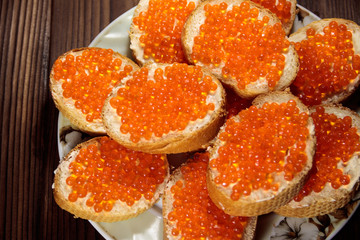 Sandwiches with butter and red caviar on wooden table